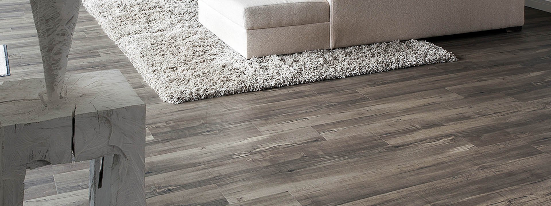 Detailansicht eines Wohnzimmers mit grauem Designboden in Holzoptik, hellem Teppich und moderner Einrichtung